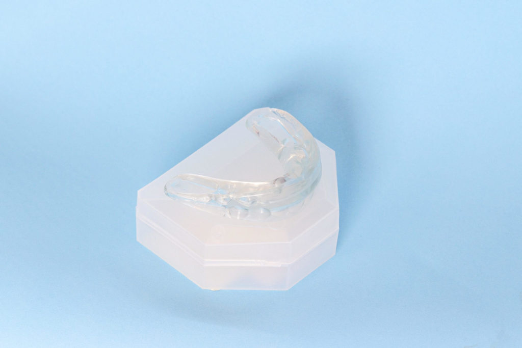 A clear mouth guard sits on a white protective case on a blue background