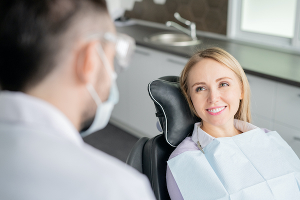 A female dental patient sits in an exam chair and smiles at the dentist